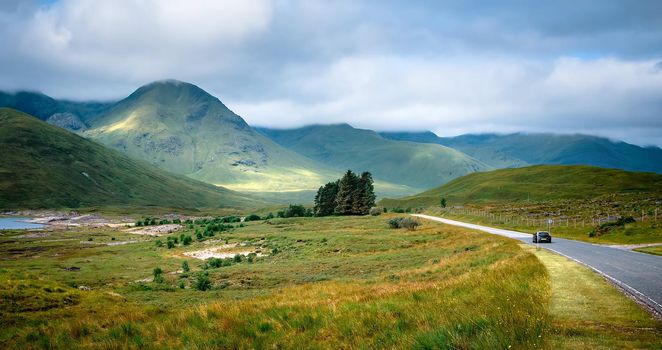 A car driving on a road in rural settings towards the mountains ahead, Cars on the road towards the mountain