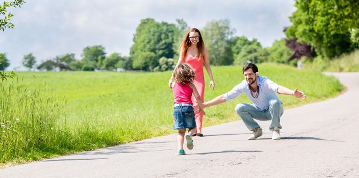 Mom, dad and daughter having walk on path in summer