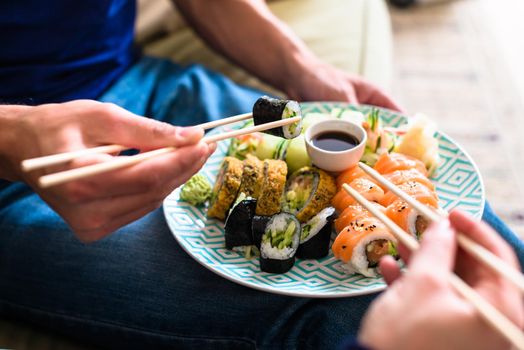 Close-up of the hands of a young couple eating traditional Japanese food with chopsticks during romantic dinner at home