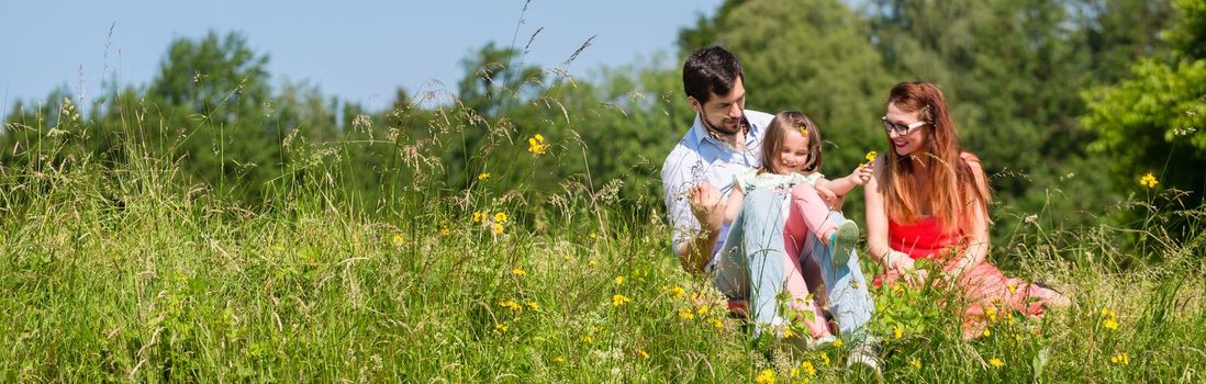 Panorama picture of family with mom, dad and daughter on meadow