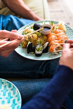 Close-up of the hands of a young couple eating traditional Japanese food with chopsticks during romantic dinner at home