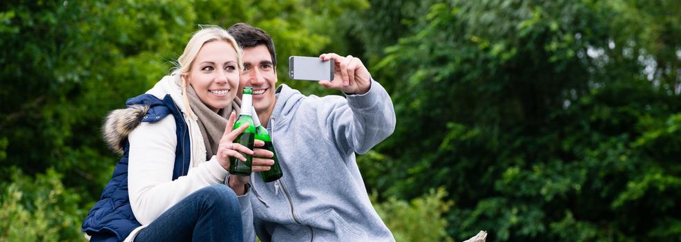 Woman and man drinking beer taking selfie while hiking in forest