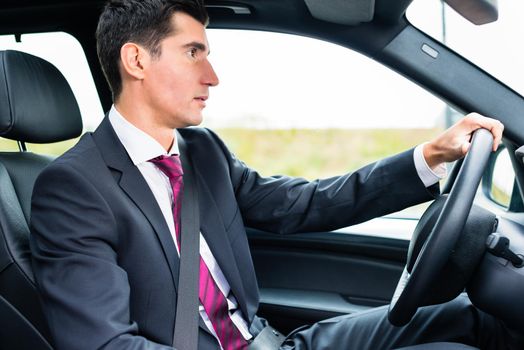 Man driving his car for business travel wearing a suit