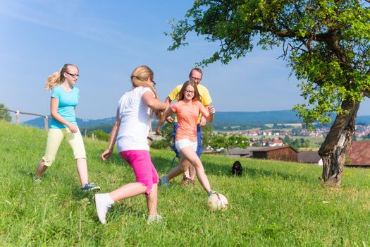 Family playing soccer on meadow in summer