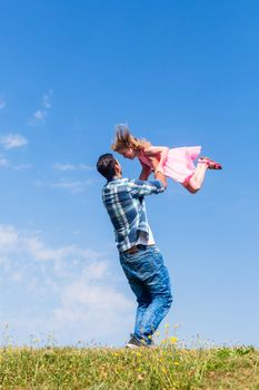 Father lifts daughter over head on summer meadow