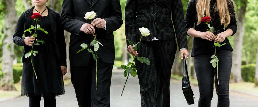 Torso of family on cemetery mourning holding red and white roses in hands