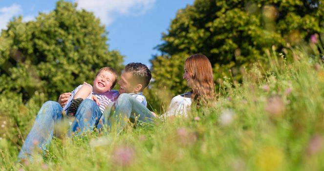 Family cuddling sitting on meadow in summer