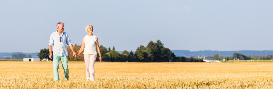 Senior woman and man holding hands having walk on field