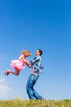 Father lifts daughter over head on summer meadow