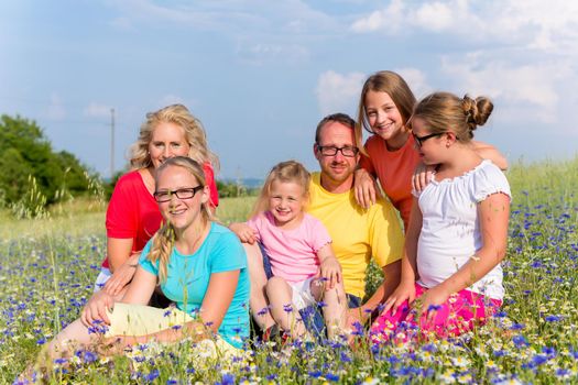 Family sitting on meadow in flowers, mom, dad and the kids