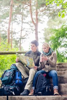 Hiking couple, woman and man, having break on a forest trail and reading the map