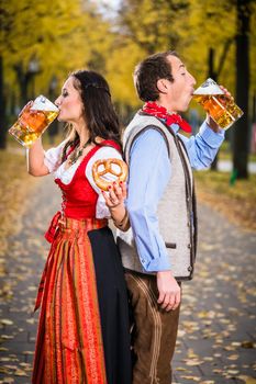 Woman and man from Austria or Bavaria standing back-to-back and drinking beer