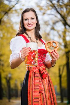 Woman in traditional Dirndl, carrying a beer mug and a Pretzel, standing