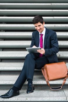 Young businessman smiling while using a tablet PC for online communication or data storage outdoors