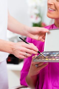 Woman in cosmetic salon receiving makeup by professional beautician