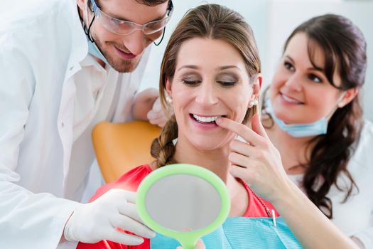 Woman after dental bleaching at dentist checking teeth in mirror