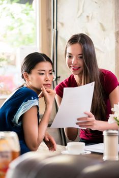 Three beautiful young women holding files while sitting in a coffee shop