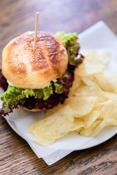 Close-up of burger with fresh green salad and potato chips served on white paper