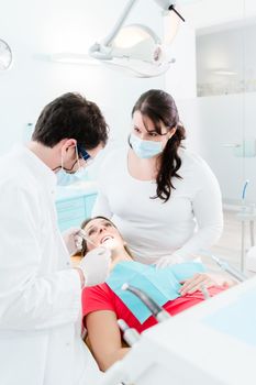 Dentist and paramedic treating pregnant woman patient in their surgery