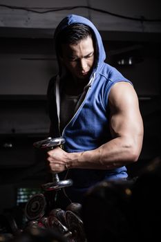 Young man wearing hoodie sweater reaching out with his hand holding a dumb-bell in gym