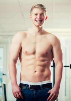 Trained athlete showing his muscles and six pack in health club gym