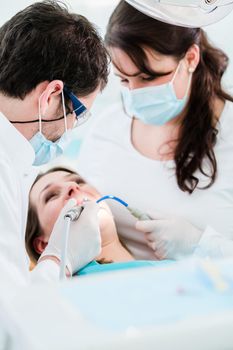 Dentist treating woman patient using drill on her teeth