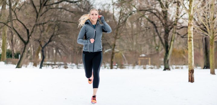Woman running or jogging down a path on winter day in park
