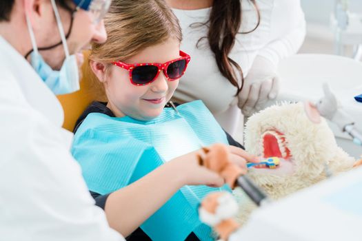 Child at dentist office looking after teeth of pet toy, the doctor relieving the kid of her fear that way