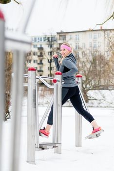 Young woman training her legs on fitness path at winter day in the park