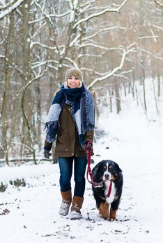 Woman with her dog hiking or walking in winter on a snow covered path