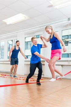 Man and women getting guidance at tightrope walking at health club gym