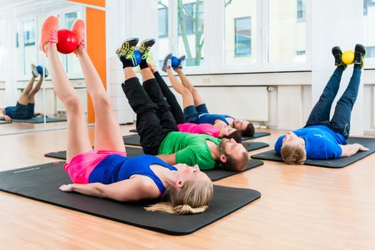 Athletes in health club doing physical exercises on floor with balls at gym