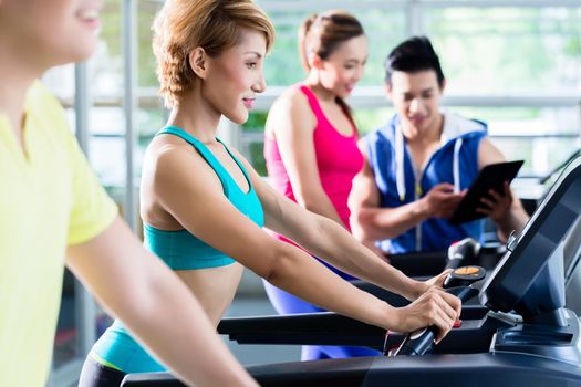 Group of sportive young people during cardio training on treadmill under supervision of trainer with tablet