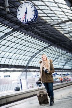 Woman looking impassionate at clock in train station as her train has a delay