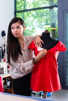 Asian tailor adjusts garment design on mannequin in studio