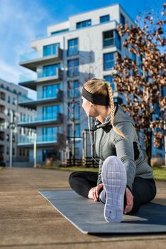 Fit young woman with a healthy lifestyle daydreaming while stretching her leg on a mat during outdoor warm-up exercises in a sunny day