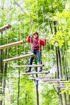 Teenage girl, walking on rope bridge in climbing course enjoying the trill of the sport