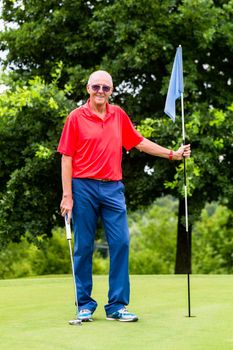 Senior man playing golf on course holding flag