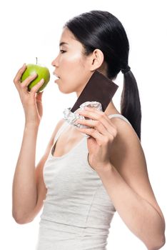 Funny young woman eating a fresh apple while looking at a chocolate bar