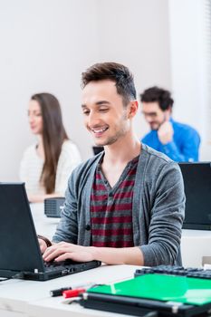 Student working on laptop PC in college, more women and men in background