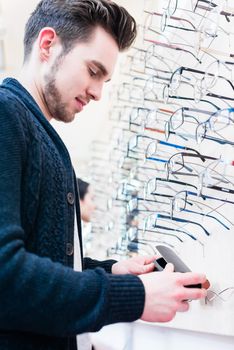 Man as customer choosing glasses from shelf in optician shop