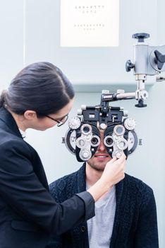 Optician and man at eye examination with phoropter in optician shop