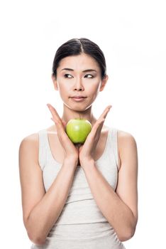 Thoughtful young Asian woman holding a green apple against white background