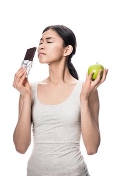 Funny young woman eating a fresh apple while looking at a chocolate bar