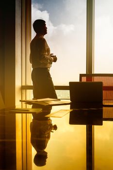 Indian business man standing on office window in pensive posture looking at city, filtered image