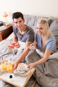 Happy young couple eating bread and strawberry jam while having breakfast in bed