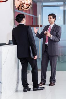 Asian executive Manager and affiliate leaning at front desk of office building and talking about business