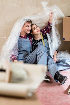 Happy young couple wearing overalls while resting and day dreaming about their future together after moving in into their new home