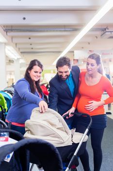 Woman, man, and sales lady in baby store testing buggy