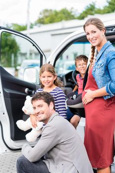 Family buying car, mother, father and child at dealership with soft toy and special kid seat